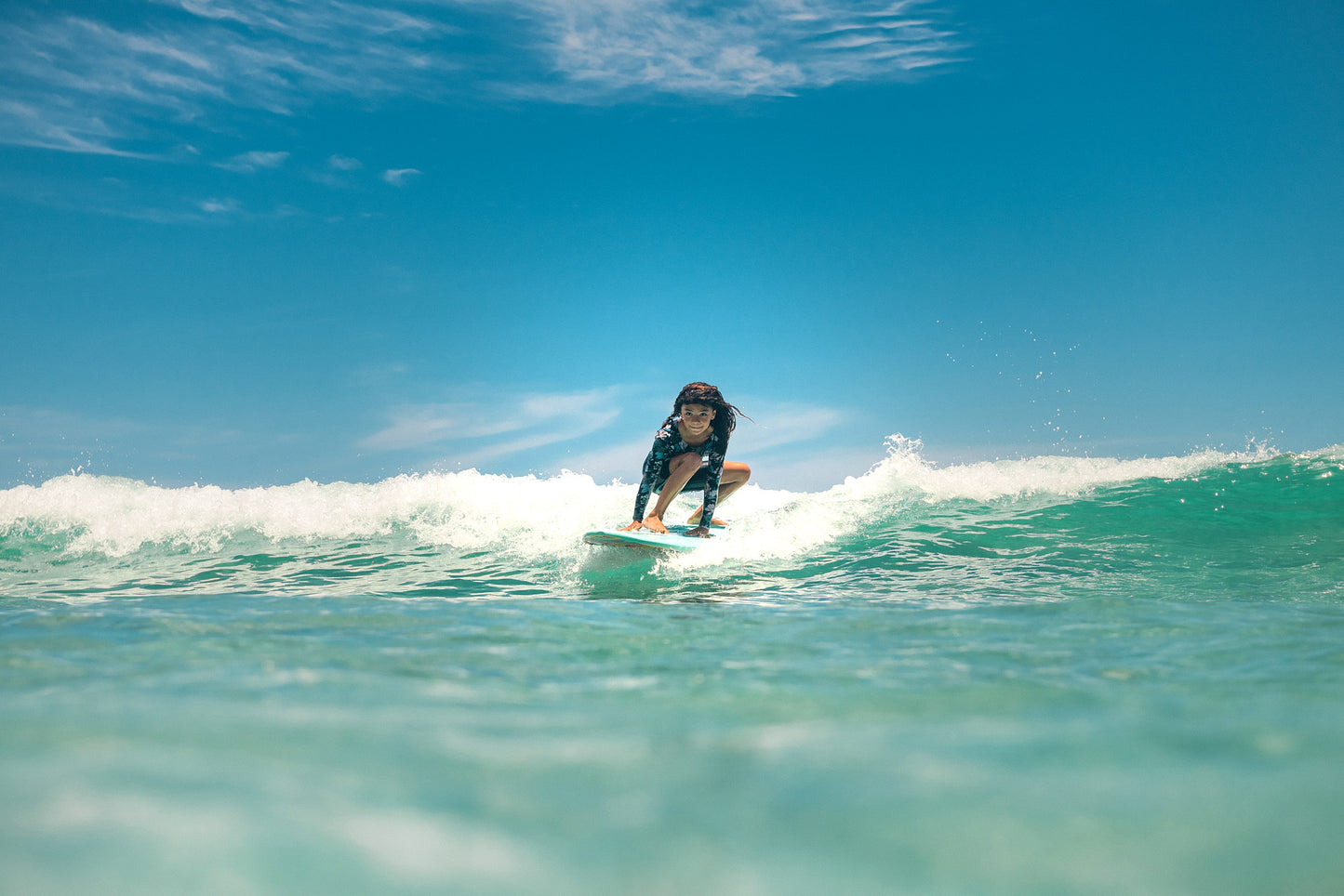 Girl surfing a Legion of Fun surfboard on a wave with clear blue sky